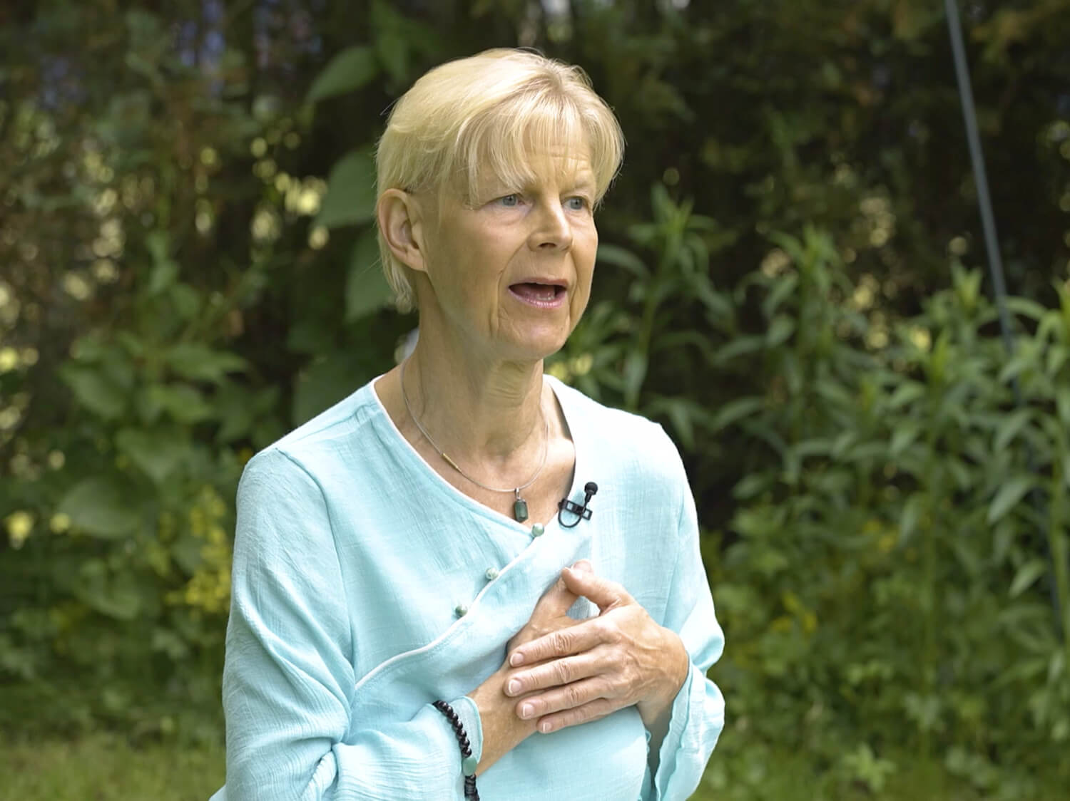 Nèizàng Ànmó – Qi-Gong-Videokurs von Annette Deinzer 6 Porträt Annette Deinzer, blonde Haare, türkises Oberteil, vor grünem Hintergrund