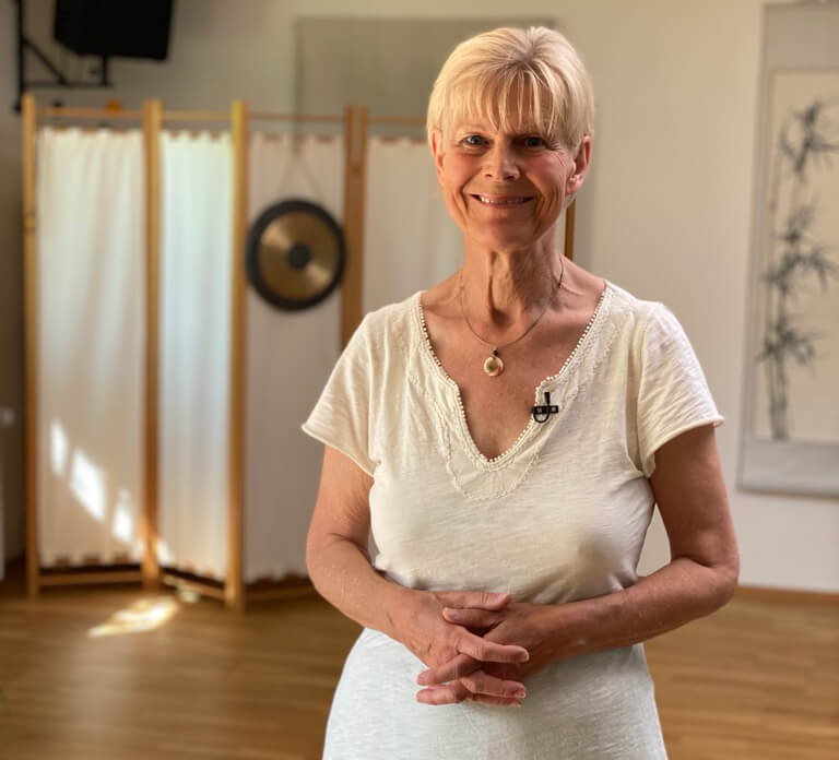 Nèizàng Ànmó – Qi-Gong-Videokurs von Annette Deinzer 7 Annette Deinzer Porträt im Therapieraum, weißes Oberteil, Schmuck, professionelle Aufnahme