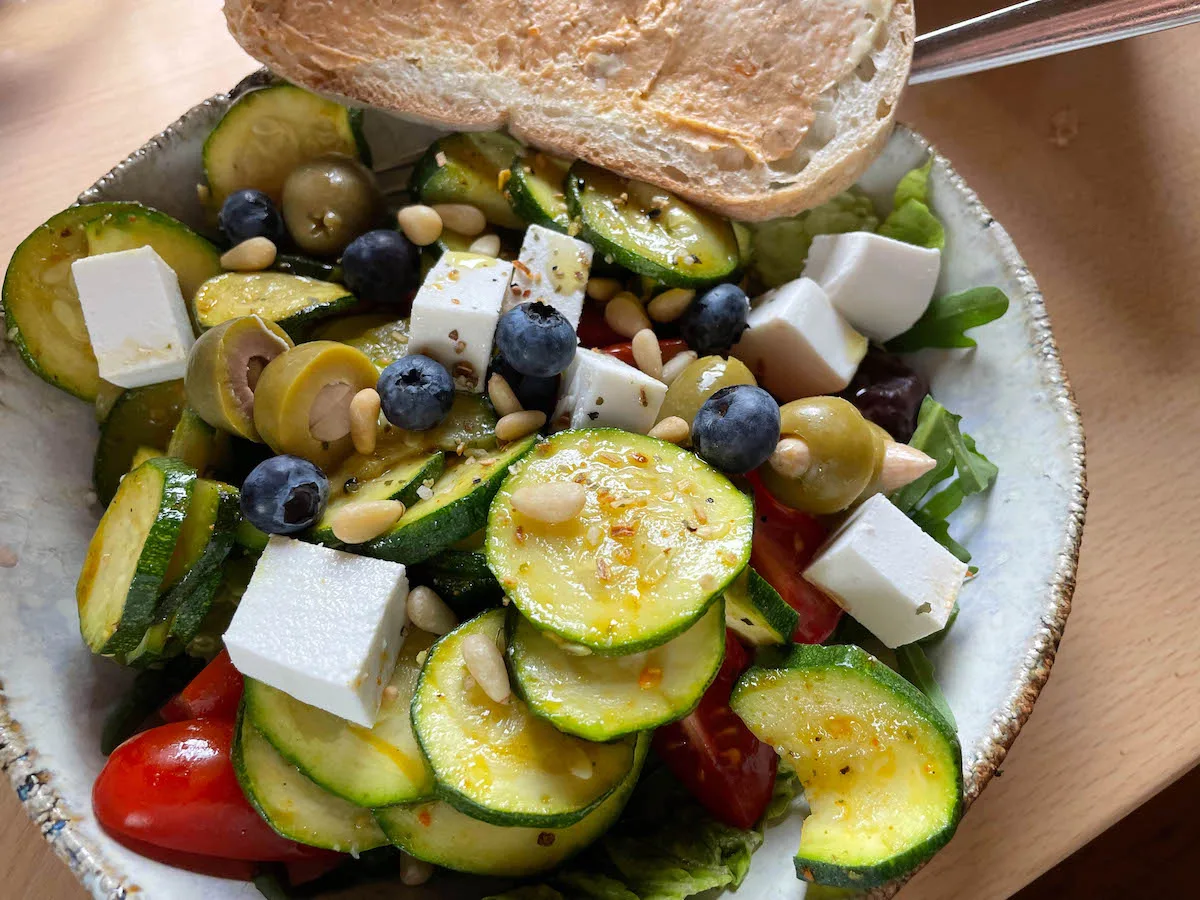 Sommersalat mit Zucchini, Feta, Oliven, Blaubeeren und Kichererbsen auf Teller mit Brot, Naturjournal Rezept von Ramona Weyde