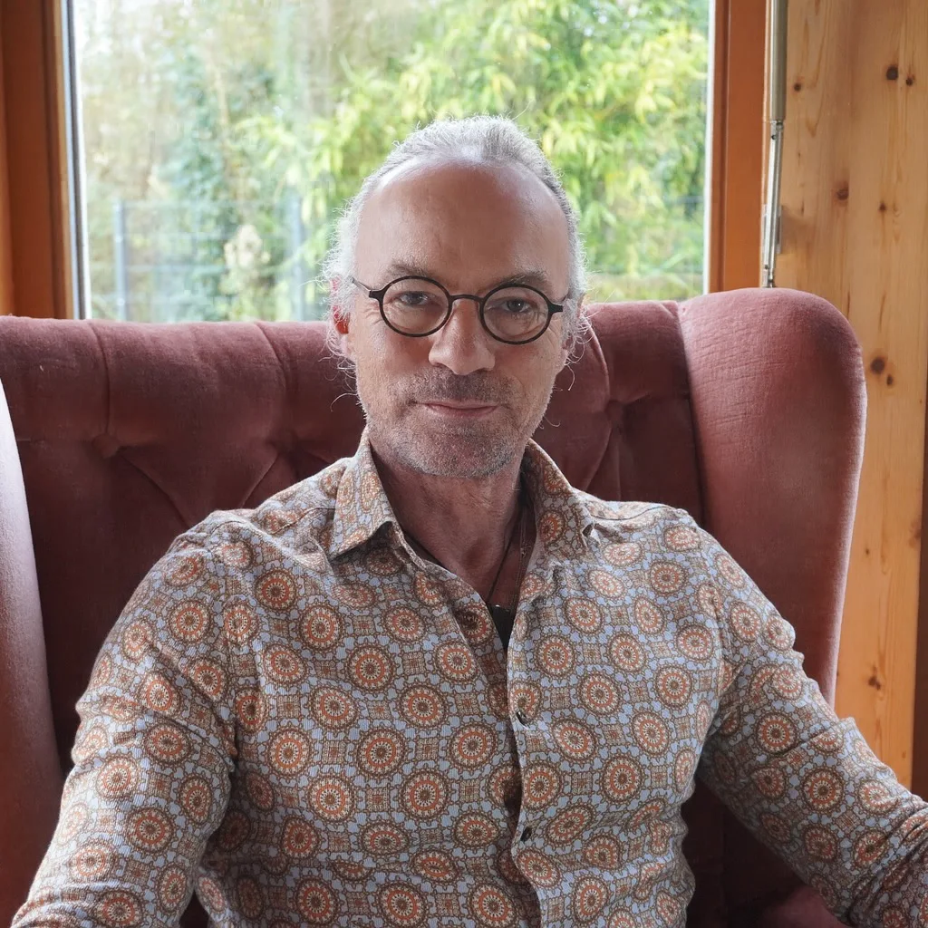 Karl Seeger sitzt in rotem Sessel mit gemustertem Hemd und Brille