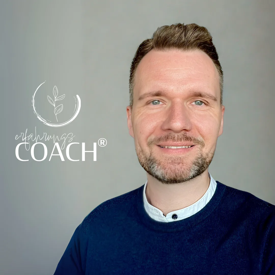 Junger Mann mit Undercut-Frisur und Bart lächelnd vor grauem Hintergrund mit erfahrung33 Coach Logo