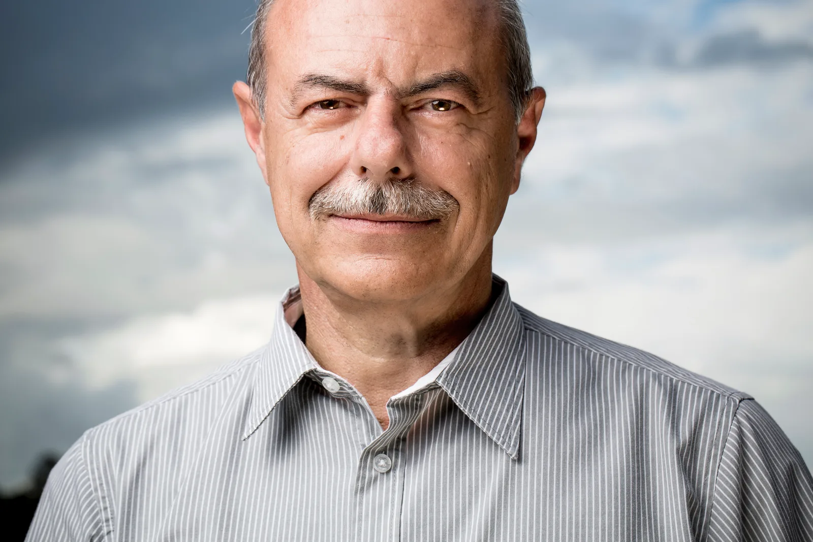 Portrait eines älteren Mannes mit Schnurrbart in gestreiftem Hemd vor Himmelshintergrund