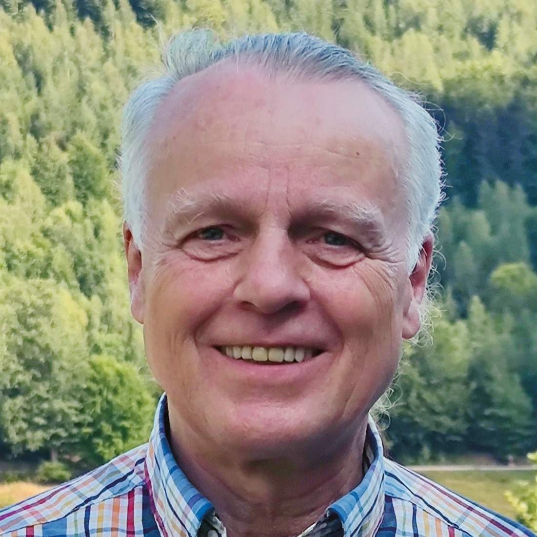 Portrait Mann lächelnd vor grünem Wald mit kariertem Hemd