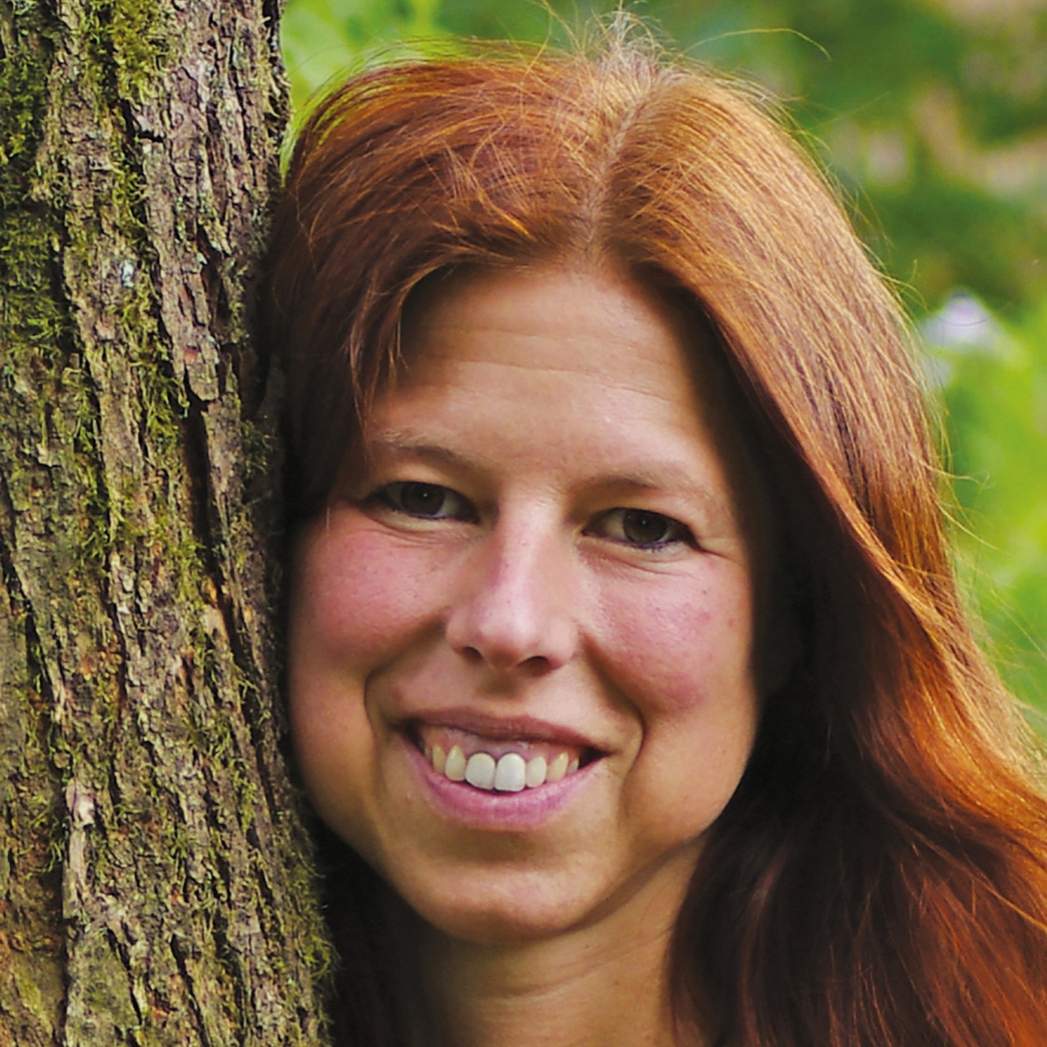Portrait Frau mit rötlichen Haaren lächelnd an Baum mit Moos