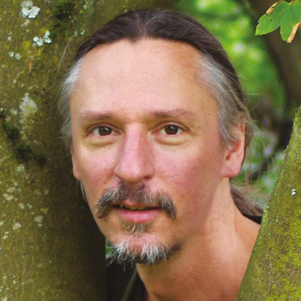 Porträt von Reiner Angermeier mit Gesichtsbehang, vor moosigem Baum