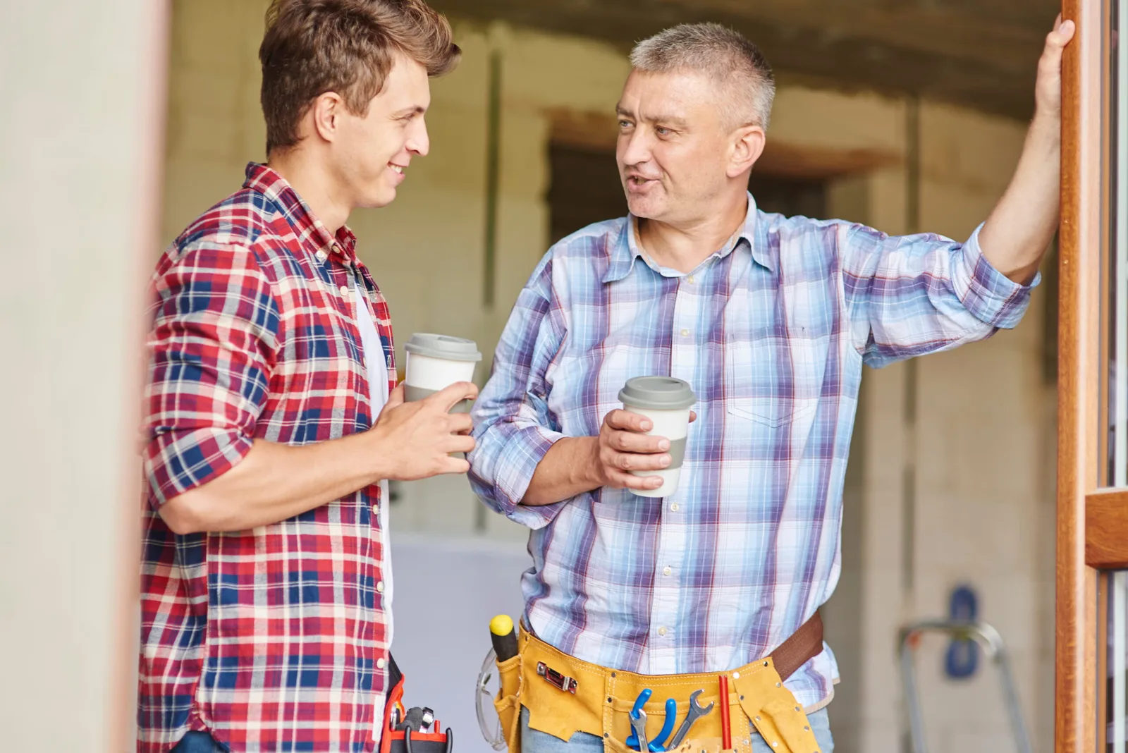 Ausbilder und Lehrling im Gespräch mit Kaffee in karierten Hemden