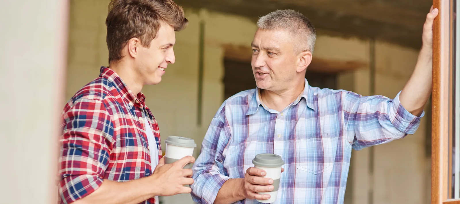 Ausbilder und Lehrling im Gespräch mit Kaffee in karierten Hemden