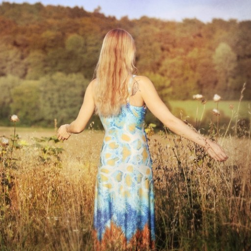 Frau mit roten Haaren von hinten in Blütenkleid in Feld und Wald