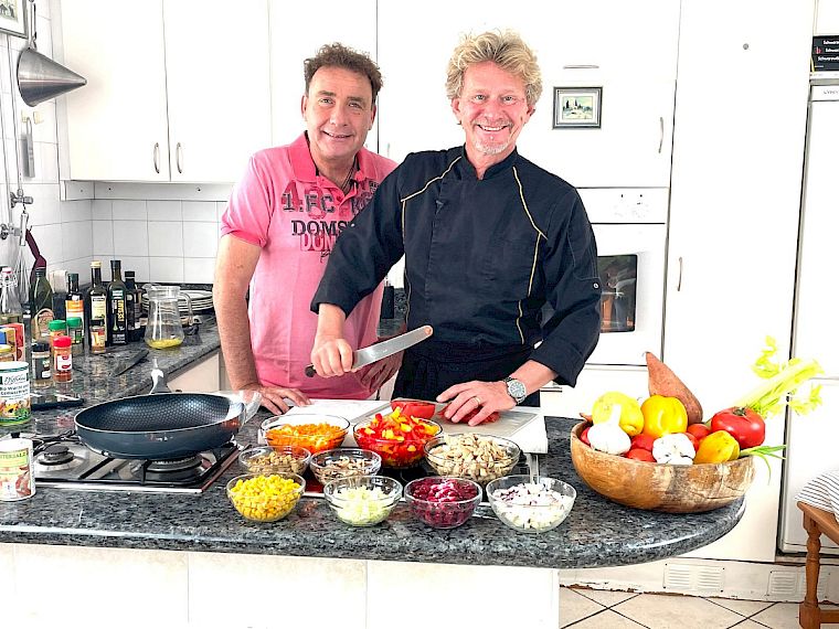 Neustart Ernährung – Basisch-Kochen-Kurs von Ralf Moll 13 Mann in rosa und Mann in blau an Küchentheke mit Gemüse-Schüsseln beim Kochen