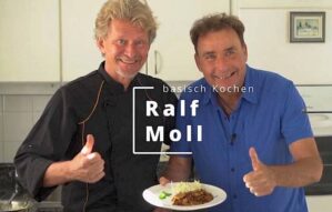 Ralf Moll und Holger Ilg in einer Küche mit einem Teller Essen, beide zeigen Daumen nach oben