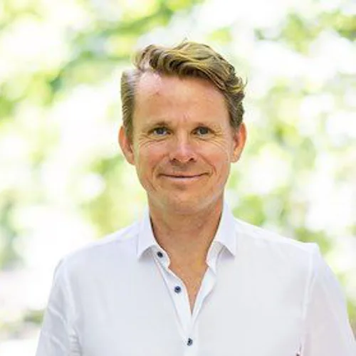 Portraitfoto von Timo Simon, Mann mit dunklem Haar, weißem Hemd, grüner Hintergrund