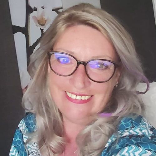 Porträt von Conny Bock, Frau mit blonden Haaren und Brille, lächelnd vor unscharfem Hintergrund