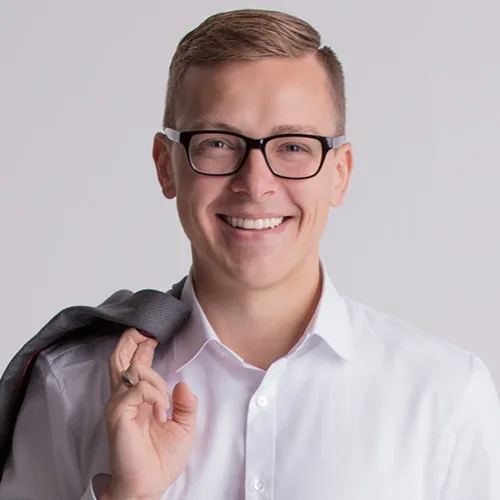 Porträt von Florian Günther, junger Mann mit Brille und hellem Hemd vor neutralem Hintergrund