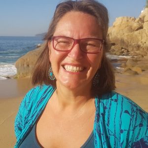 Porträt Amata Bayerl, Frau mit Brille am Strand vor Felsen