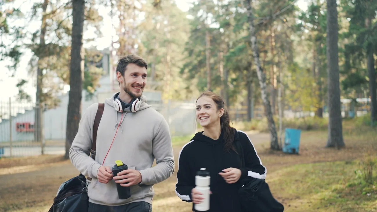 Zwei Menschen gehen mit Sporttaschen durch einen sonnigen Park als Symbol für einen gemeinsamen Neustart
