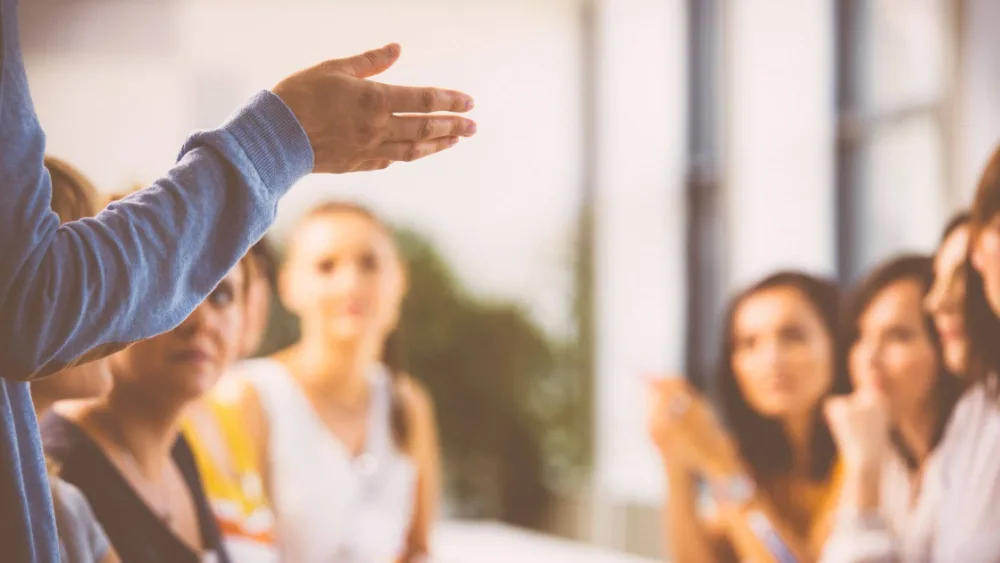 Trainer präsentiert vor Gruppe von Teilnehmern mit ausgestreckter Hand, NLP-Seminar Atmosphäre