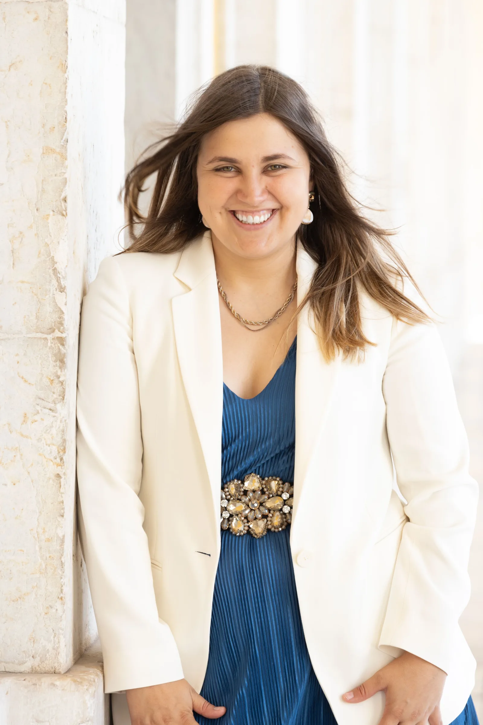 Carolin Mallmann, NLP-Trainerin, lächelnd in weißem Blazer und blauem Kleid mit Gürtel