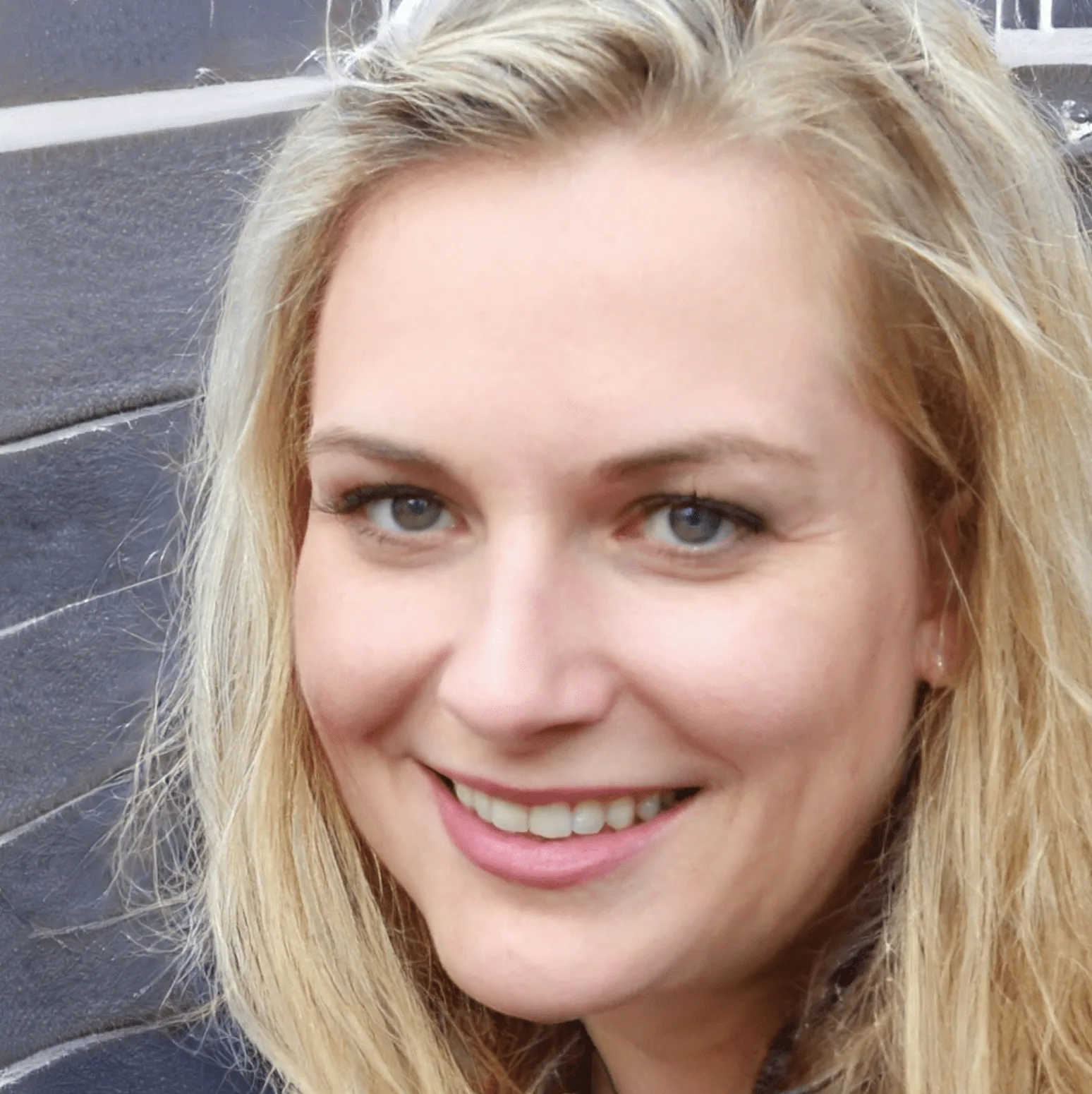 Blonde Frau lächelt in die Kamera vor Backsteinwand-Hintergrund