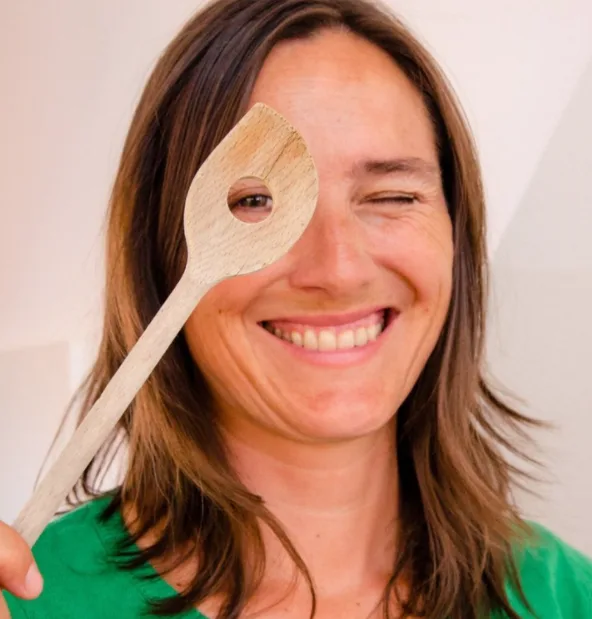 Martina Tripold-Pratscher mit Holzkochlöffel vor Gesicht, grünes Shirt, lachend