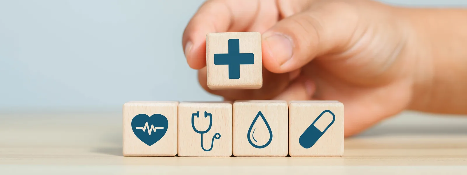 Hand platziert Holzwürfel mit Plus auf Würfel mit Herz-, Stethoskop-, Wasser- und Pflaster-Icon