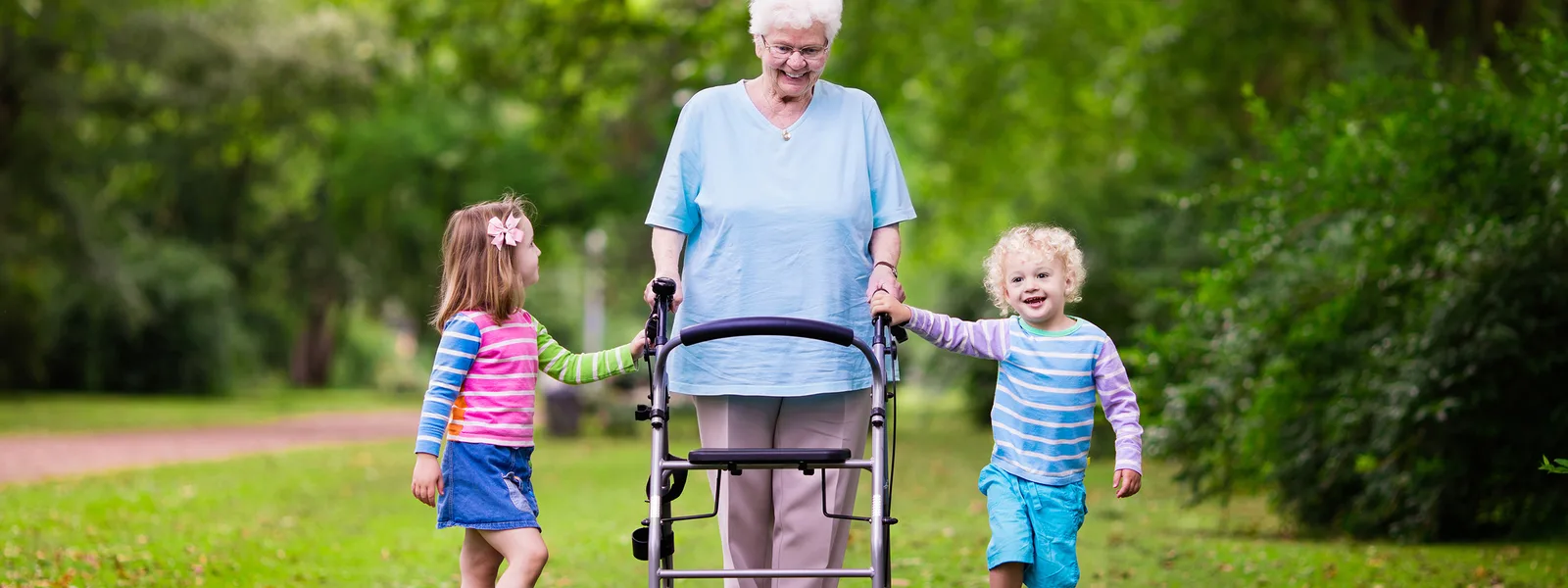 Großmutter mit Kinderwagen und zwei Kindern im grünen Park spazierend