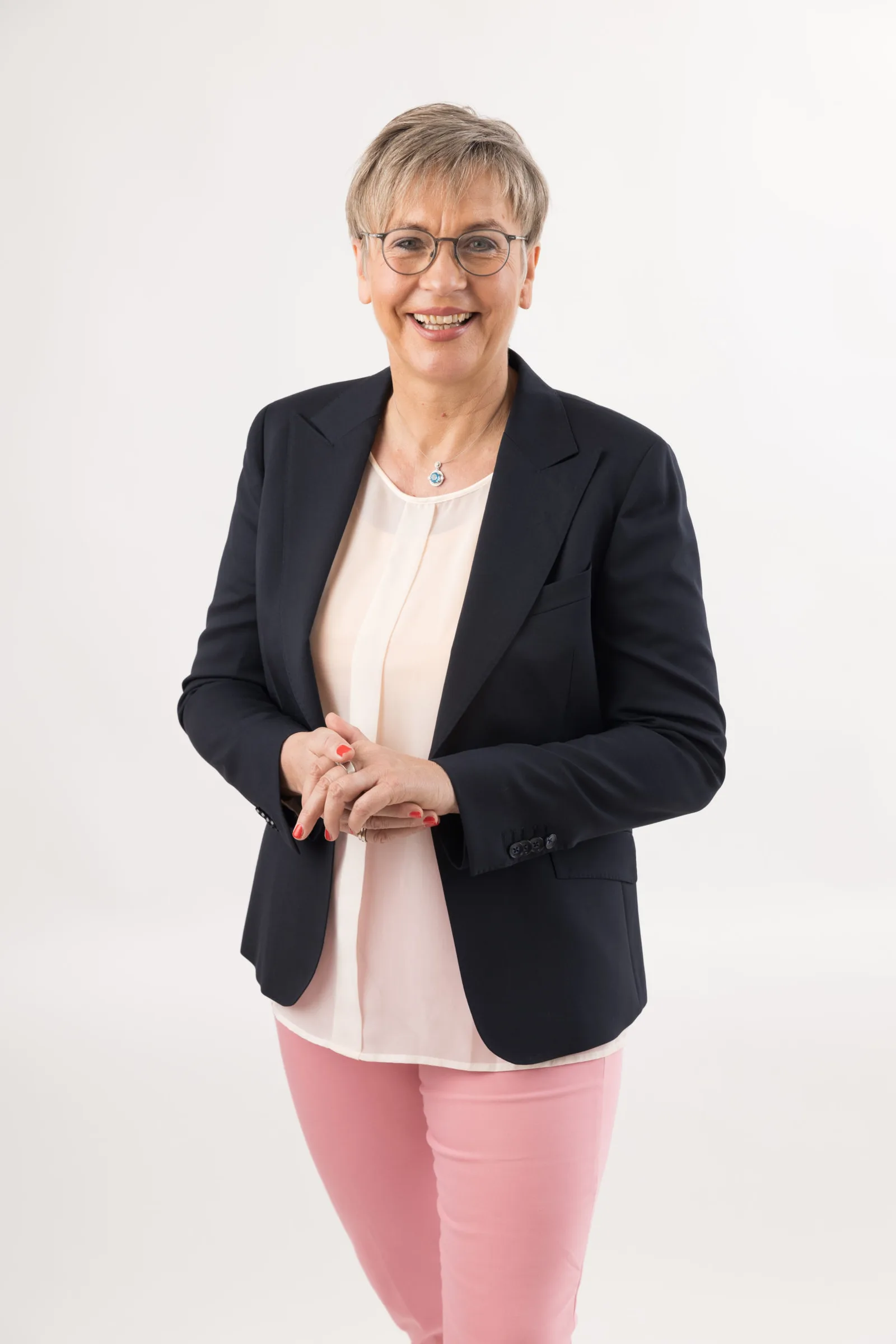 Porträt lächelnde Frau mit Brille, schwarzem Blazer über rosa Top und rosa Hose