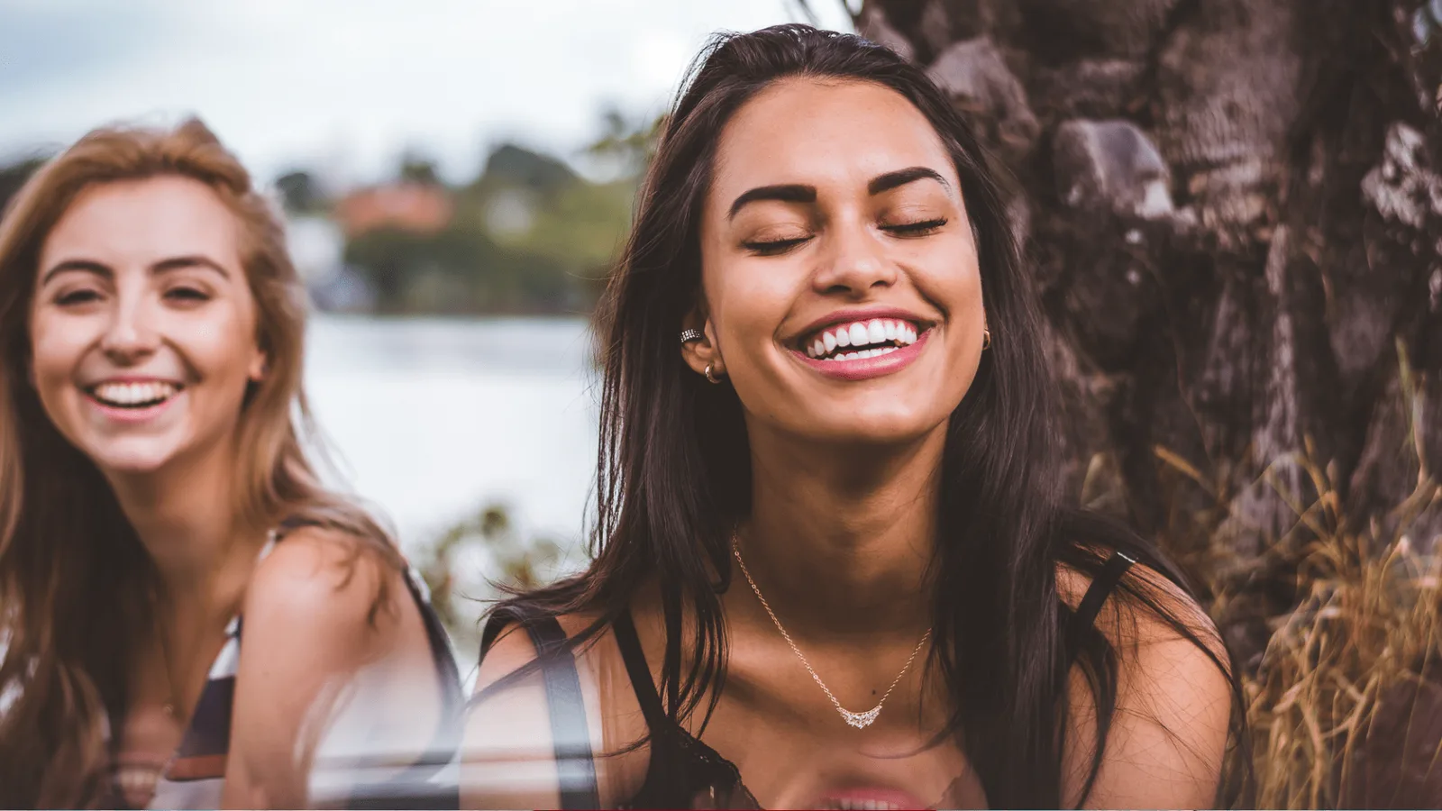 Zwei lachende Frauen in Nahaufnahme vor Wasser und Natur – glückliche Kundenstimme