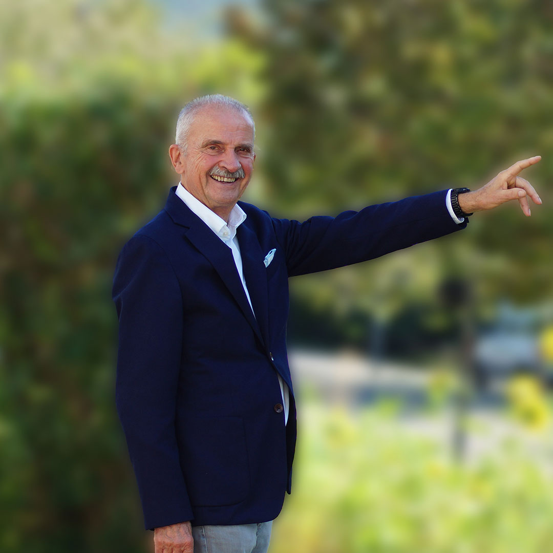 Michael Zacharias Portrait mit blauem Sakko und grünem Hintergrund, zeigt Geste