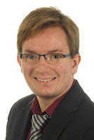 Porträtfoto eines Mannes mit Brille und Blazer, lächelnd