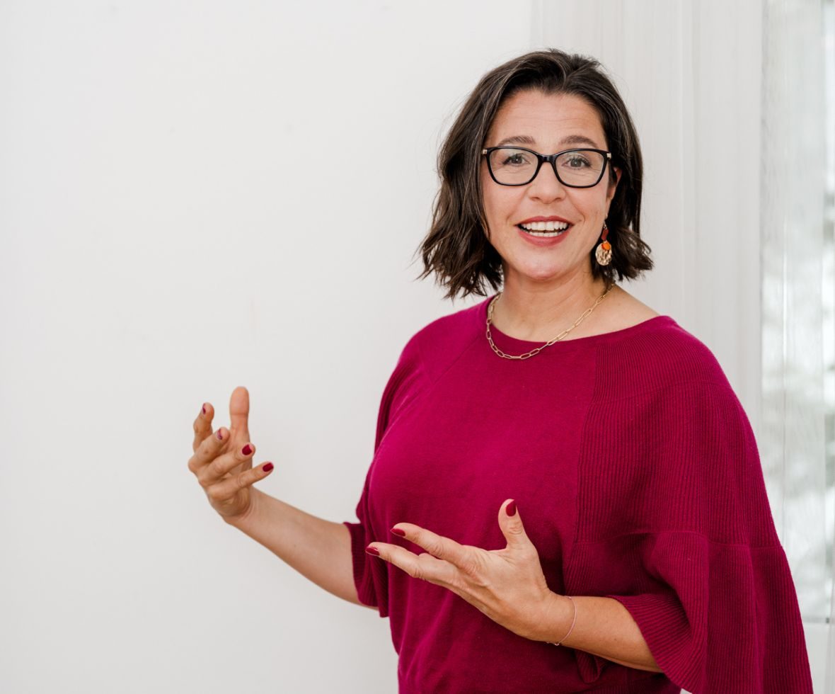 OTRANG – Trainer-Onlinekurs Rückbildung von Dr. Iris Floimayr-Dichtl 4 Dr. Iris Floimayr-Dichtl in Magenta-Pullover gestikulierend, lächelnd mit Brille und Schmuck