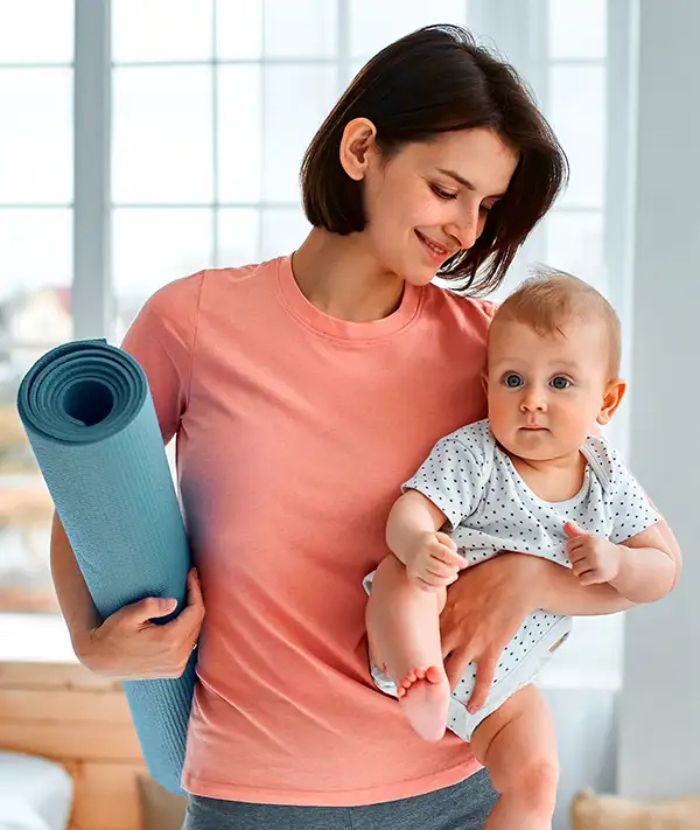 OTRANG – Trainer-Onlinekurs Rückbildung von Dr. Iris Floimayr-Dichtl 8 Junge Mutter mit Baby und blauer Yogamatte vor hellem Fenster