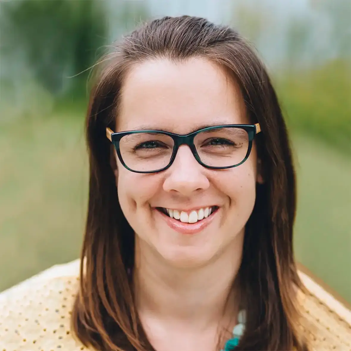 OTRANG – Trainer-Onlinekurs Rückbildung von Dr. Iris Floimayr-Dichtl 23 Porträt einer Frau mit Brille und gelbem Oberteil, Outdoor-Hintergrund