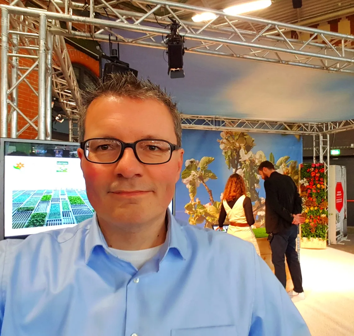 Mann mit Brille in blauem Hemd auf einer Ausstellung mit Pflanzendekoration