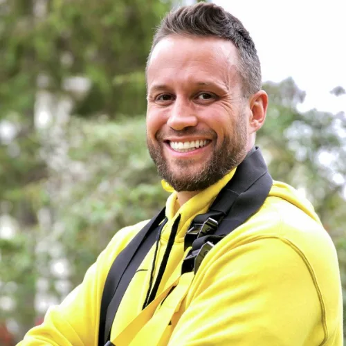 Porträt eines lachenden Mannes mit Bart in gelber Jacke vor grünem Hintergrund