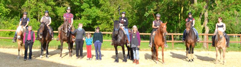Gruppe von Reitern mit Pferden und Personen zu Fuß stehen in Reitplatz mit Zaun, grüne Wald-Kulisse