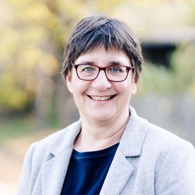 Porträt Kathrin Kaschura mit Brille und grauer Jacke über dunklem Oberteil, Außenaufnahme