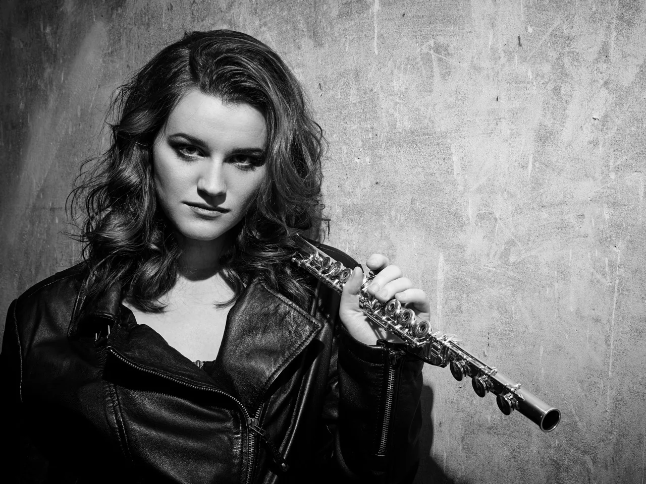 Schwarz-Weiß-Porträt der Flötistin Saskia Worf mit Flöte und Lederjacke vor Betonwand