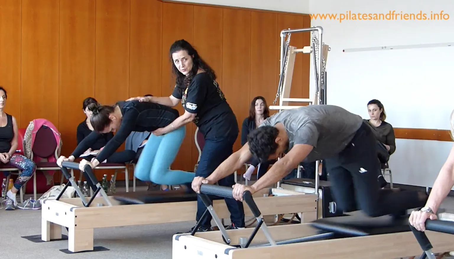 Trainerin unterrichtet Reformer-Pilates, zeigt Bewegungsabläufe an verschiedenen Geräten