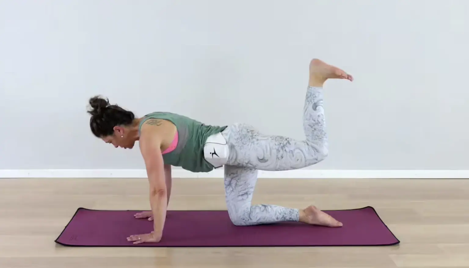 Frau in Sportkleidung führt Pilates-Übung durch: Bird Dog Position auf violetter Matte