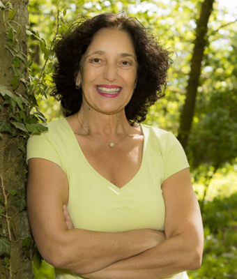 Uschi Eichinger Portrait, Frau mit dunklen Haaren in gelbgrünem Top vor Baum