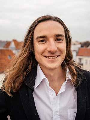 Robin Portrait, Person mit langen braunen Haaren im schwarzen Blazer vor Dächer