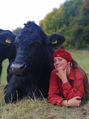 Rosina Portrait, Frau in roter Jacke und Kopftuch neben schwarzer Kuh auf Wiese