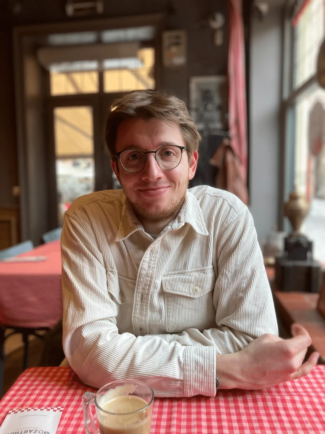 Maximilian Schollemann in beiger Hemdbluse sitzt lächelnd an Tisch mit Kaffee