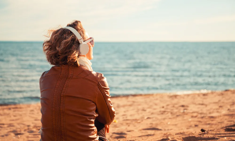 Frau mit Headphones blickt zum Meer am Strand in die Ferne