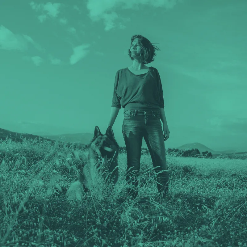 Frau mit Schäferhund in Landschaft unter türkisem Himmel