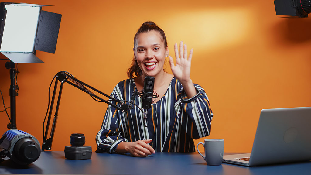 PPT Mirror Online – Software zum Folien-Spiegeln 3 Frau im Studio beim Videodreh mit Teleprompter, Mikrofonständer und Studiobeleuchtung vor orangegelbem Hintergrund