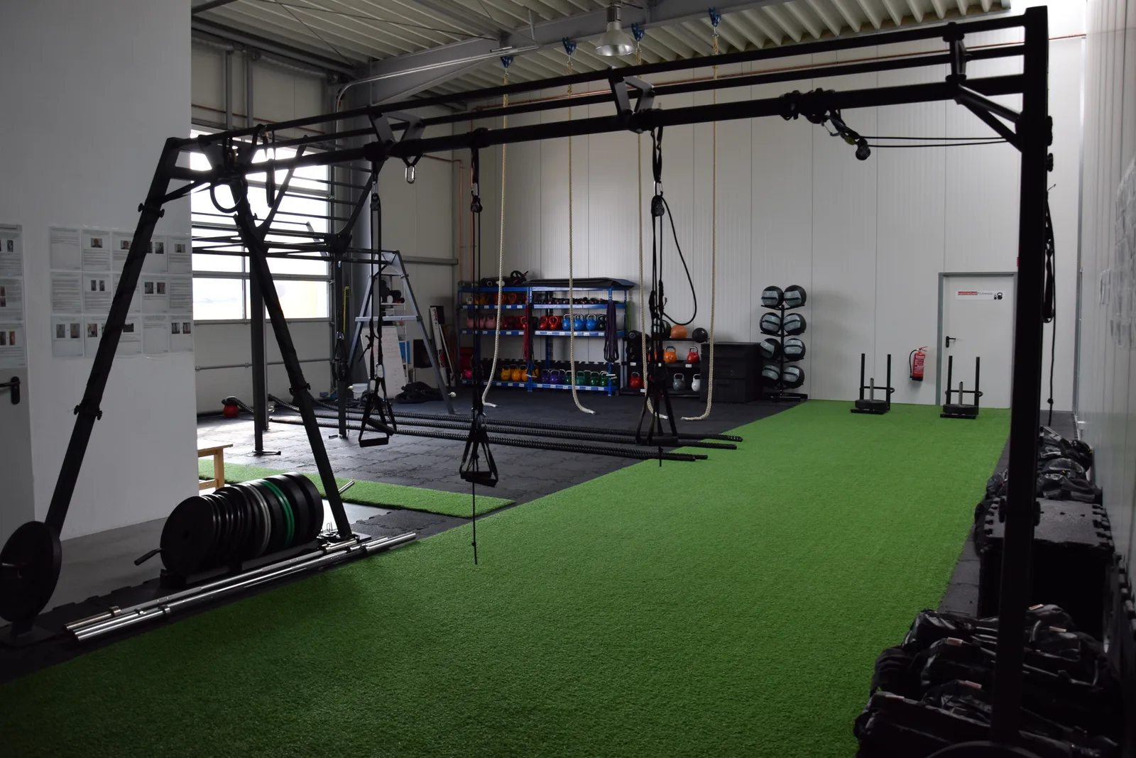 Modernes Trainingsstudio mit schwarzen Trainingsgeräten, grünem Kunstrasen und professioneller Ausstattung