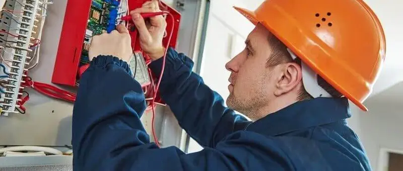Elektrofachkraft in Schutzhelm bei Wartungsarbeiten an Schaltkasten mit Sicherungsanlage