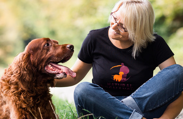 Frau mit Brille streichelt braunen Hund auf Wiese