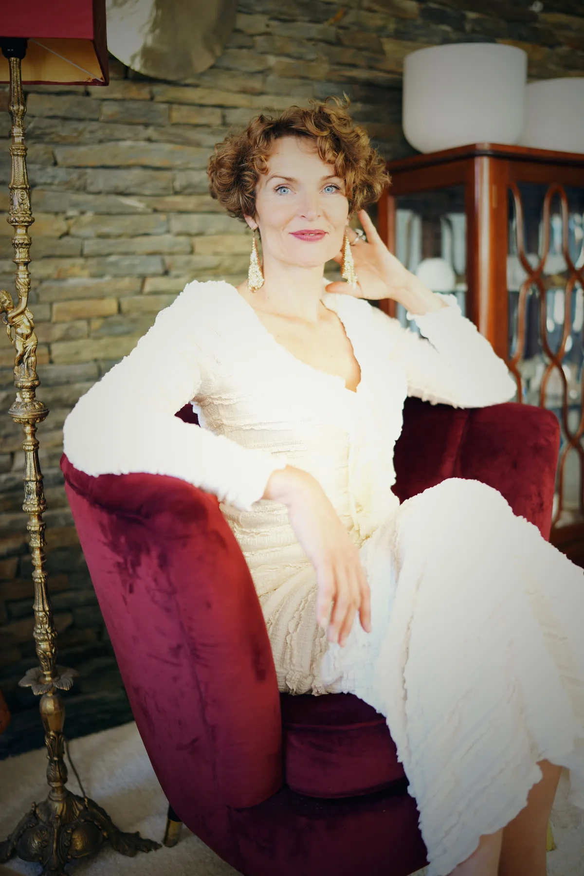 Stefanie Bruns sitzt in elegantem weißem und burgunderrotem Outfit auf Sessel in luxuriösem Interieur